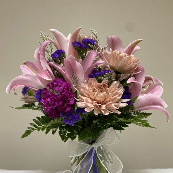 Pink lilies and peach chrysanthemums in a glass vase with a ribbon
