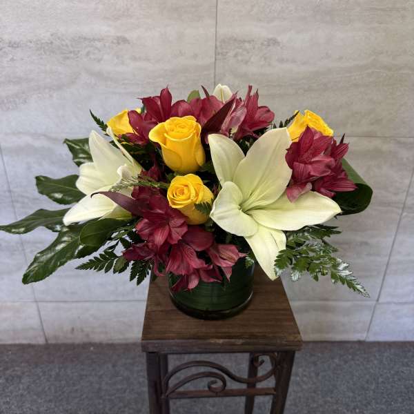Bouquet of yellow roses and white lilies with burgundy flowers in a dark vase
