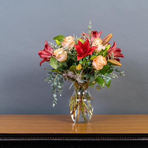Bouquet of red lilies and peach roses in a clear glass vase