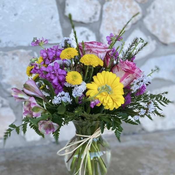 Mixed bouquet of pink, yellow, and purple flowers in a glass vase