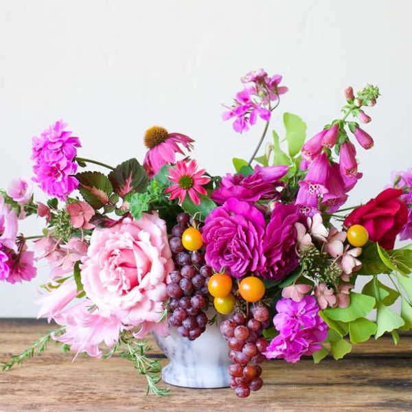 Bright pink floral arrangement with grapes and yellow berries in a white vase