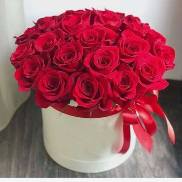 Round box of red roses topped with a red satin ribbon bow
