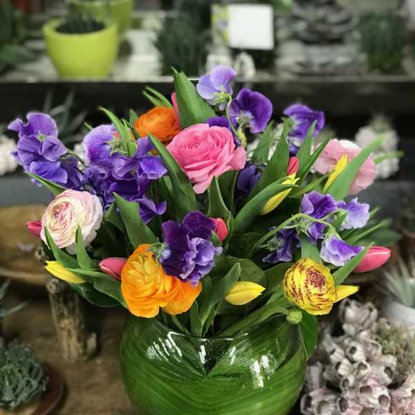 Colorful bouquet of pink, purple, yellow, and orange flowers in a green glass vase
