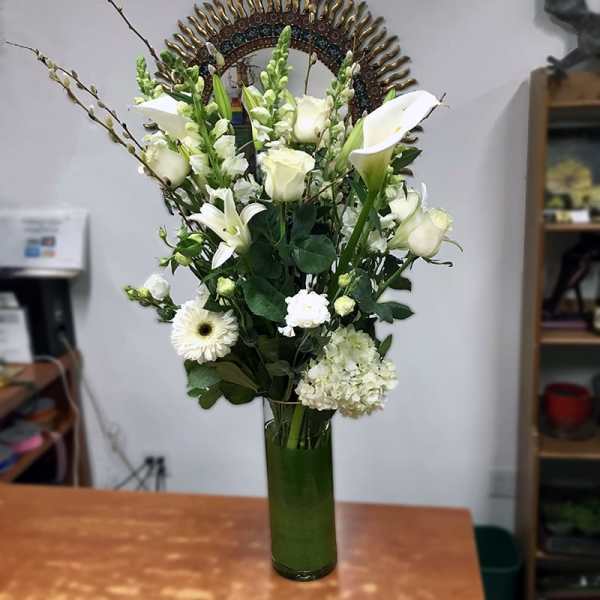 White floral arrangement in a tall green glass vase