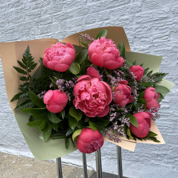 Bouquet of bright pink peonies wrapped in pastel paper
