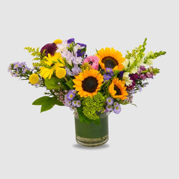 Mixed bouquet with sunflowers, purple blooms, and a glass vase
