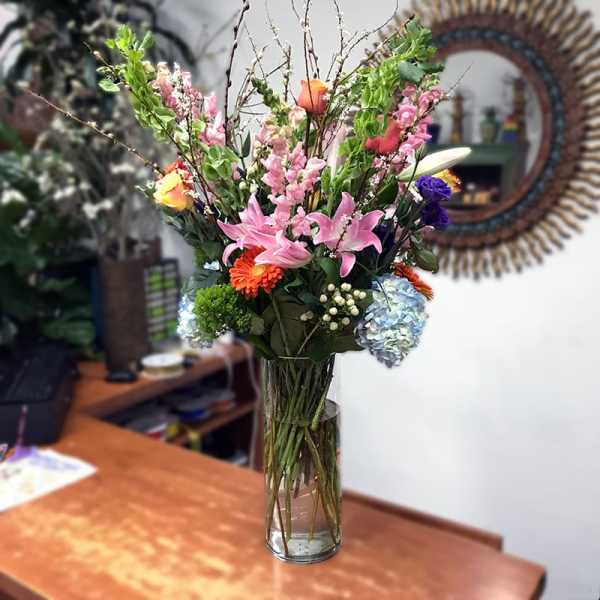 Tall mixed bouquet in a clear glass vase with pink lilies and assorted blooms