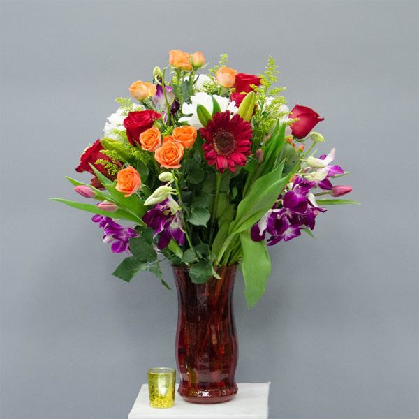 Mixed bouquet of roses, lilies, and orchids in a red glass vase