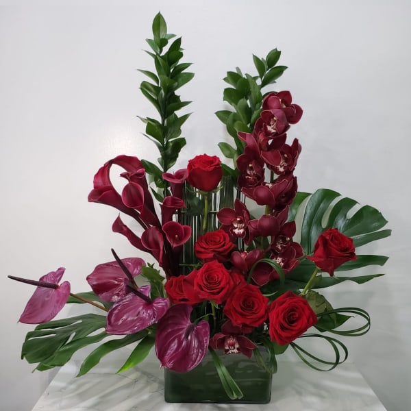 Red roses and burgundy orchids arranged in a glass vase