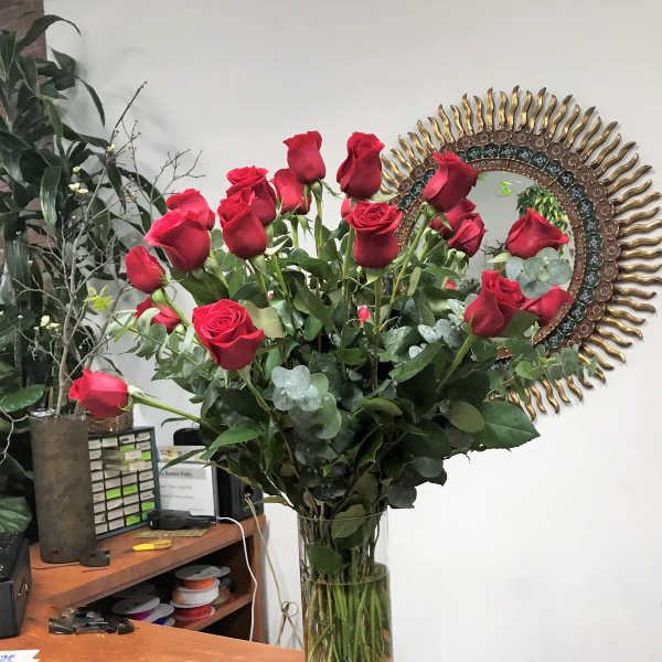 Tall vase of red roses with eucalyptus on a desk