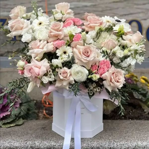 Large pastel bouquet of roses, daisies, and white blooms in a white box with ribbon