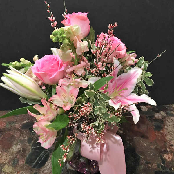Pink roses and lilies in a glass vase with a pink ribbon