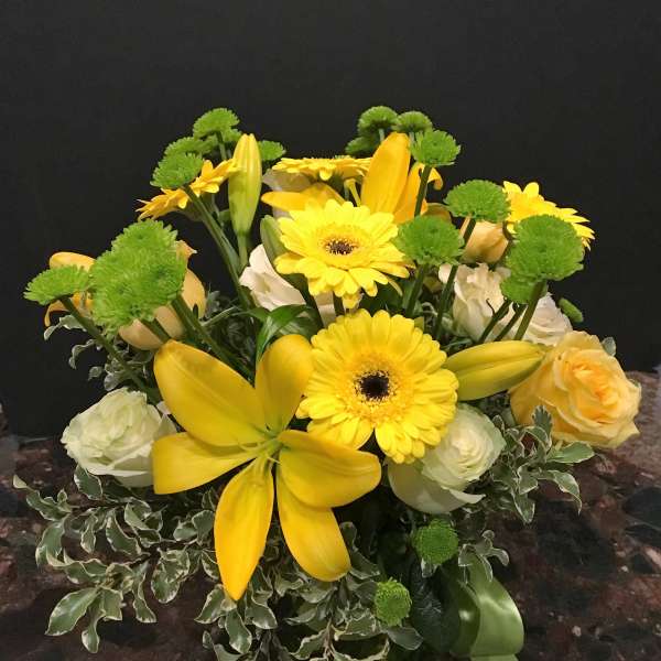 Yellow lilies and gerbera daisies with green button mums in a vase
