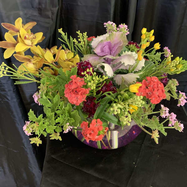 Mixed floral arrangement in a clear glass bowl with yellow orchids and pink blooms