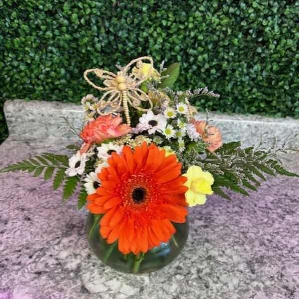 Orange gerbera daisy arrangement in a glass vase with small white flowers