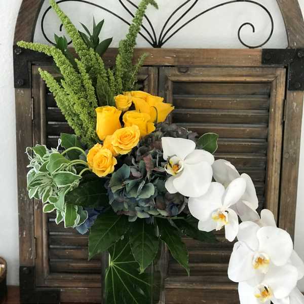 Yellow roses and white orchids in a glass vase with mixed greenery
