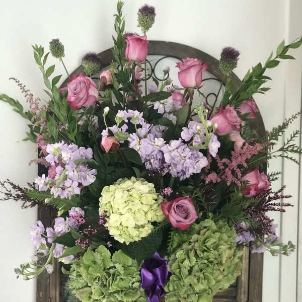 Pink roses and lavender flowers in a tall vase with green hydrangeas