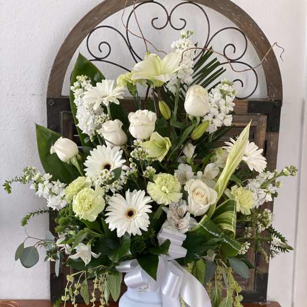 White floral arrangement in a pale blue vase with a white ribbon