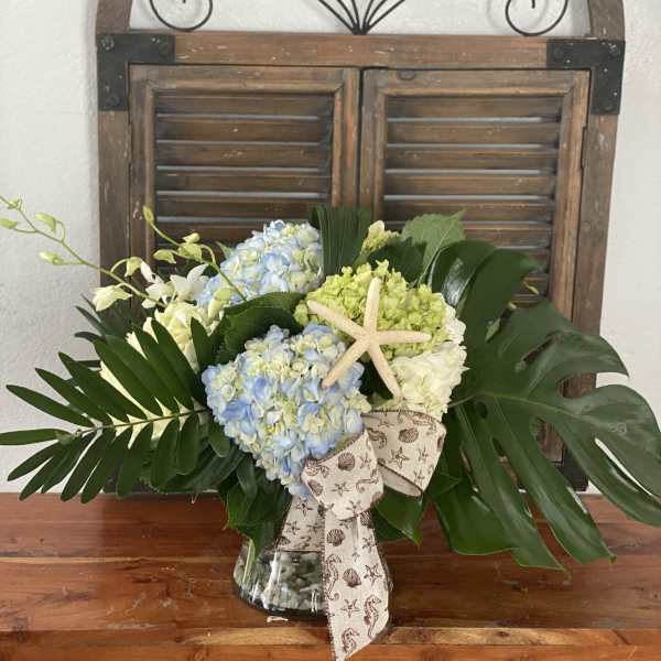 Hydrangea arrangement in a glass vase with a starfish accent and ribbon