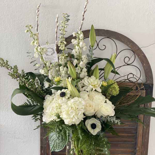 White floral arrangement in a clear glass vase with tall stems and greenery