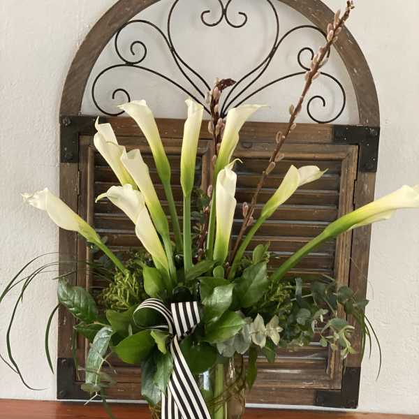 White calla lilies in a glass vase with a striped ribbon