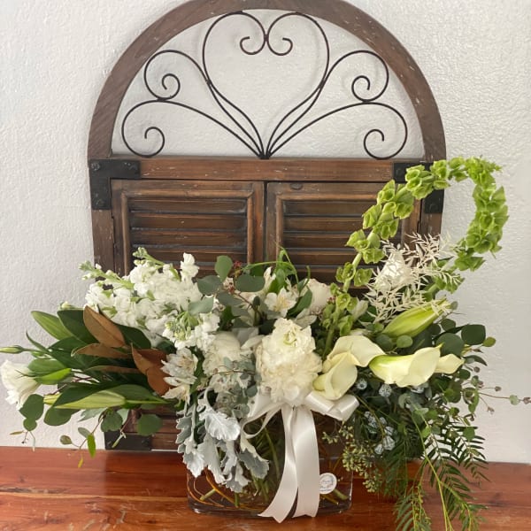 White floral arrangement in a glass vase with a ribbon