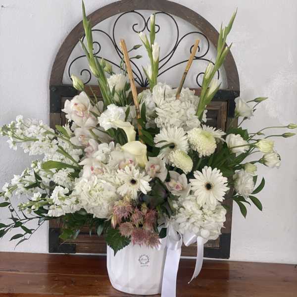 White floral arrangement in a white container with ribbon
