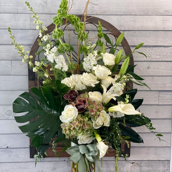 Tall white floral arrangement in a glass vase with a sage ribbon
