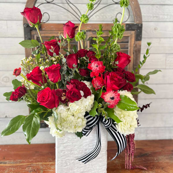 Red roses and white hydrangeas in a white vase with a striped ribbon