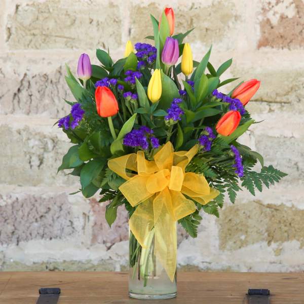 Bouquet of multicolored tulips with purple filler in a glass vase