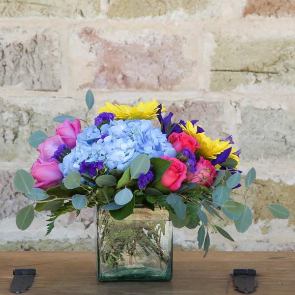 Colorful bouquet in a square glass vase with roses, hydrangea, and sunflowers