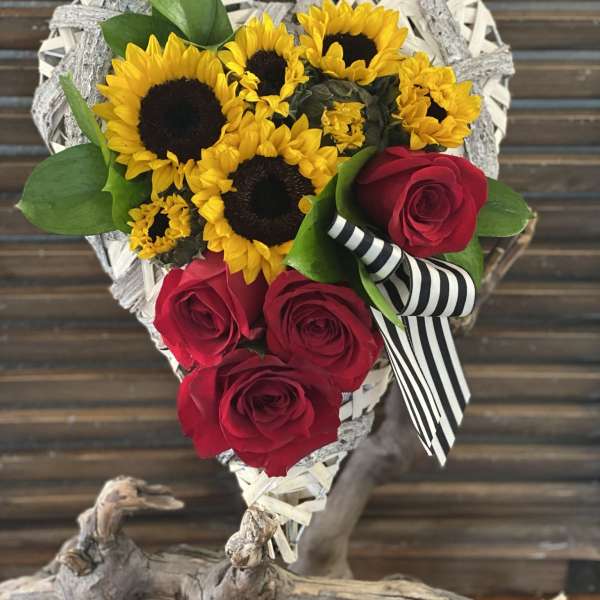 Heart-shaped bouquet of sunflowers and red roses with a striped ribbon