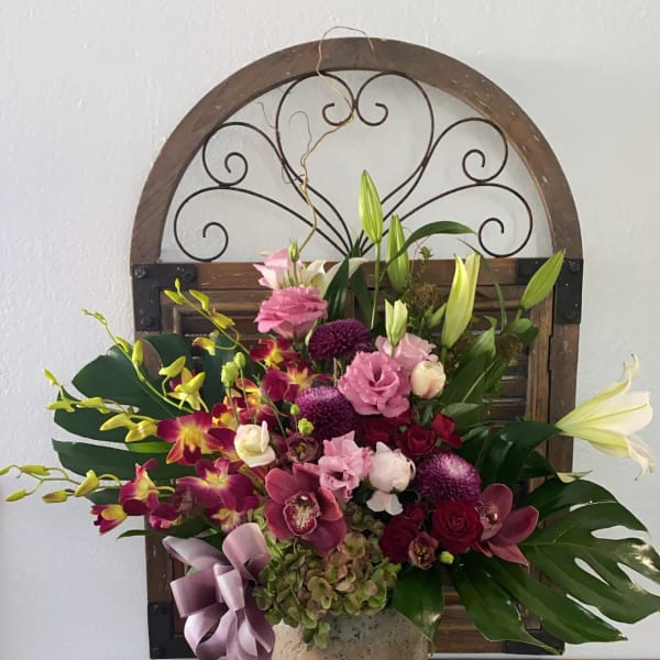 Mixed pink and purple floral arrangement in a stone vase with a ribbon