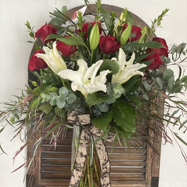Red roses and white lilies in a clear glass vase with a ribbon