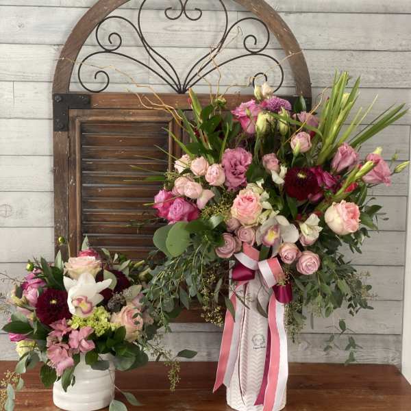 Two pink floral arrangements in white vases with ribbon accents
