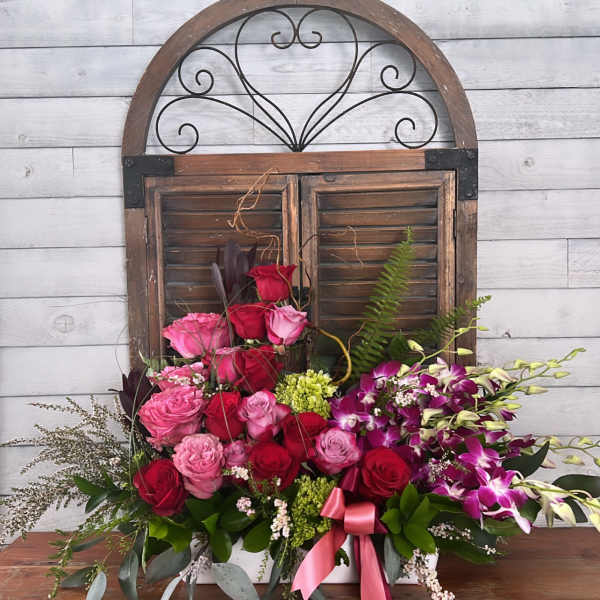 Mixed pink and red roses with purple orchids in a white container