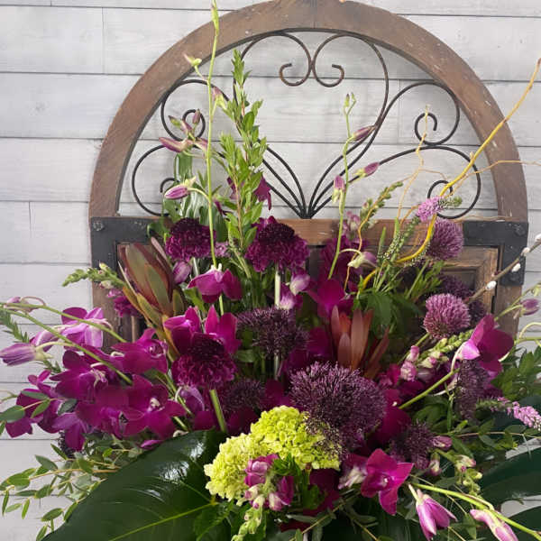 Tall magenta orchid arrangement in a white vase with a ribbon