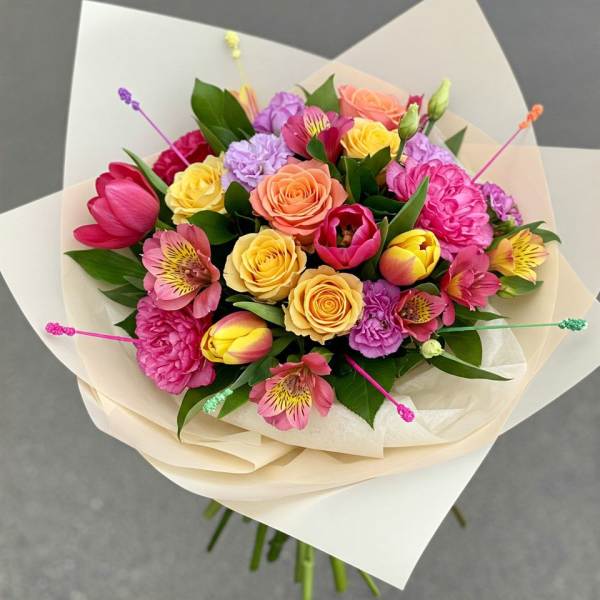 Bouquet of pink, yellow, and peach flowers wrapped in cream paper