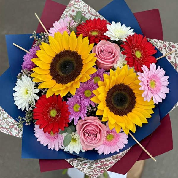Bouquet of sunflowers, gerbera daisies, and pink roses wrapped in colorful paper