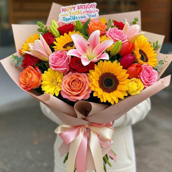Colorful bouquet of roses, lilies, and sunflowers wrapped in pink paper