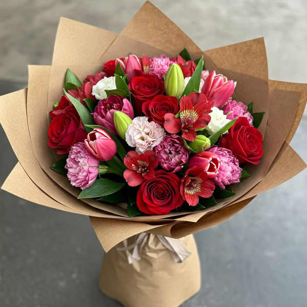 Bouquet of red roses, pink tulips, and red alstroemeria wrapped in brown paper