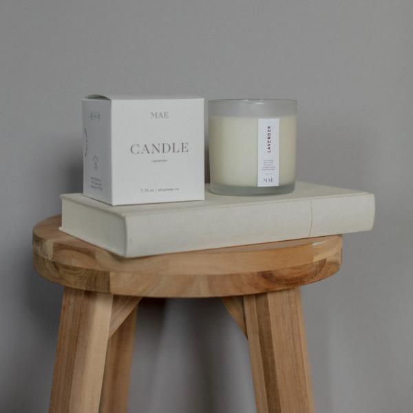 Lavender candle in a glass jar beside its white box on a wooden stool