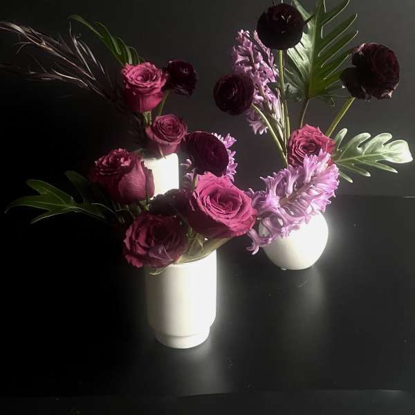 Two floral arrangements in white vases with pink and burgundy blooms