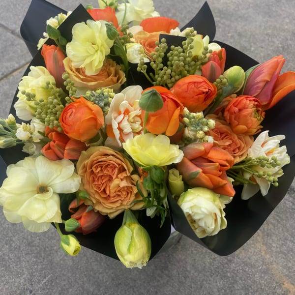 Bouquet of orange, cream, and pale yellow flowers wrapped in black paper