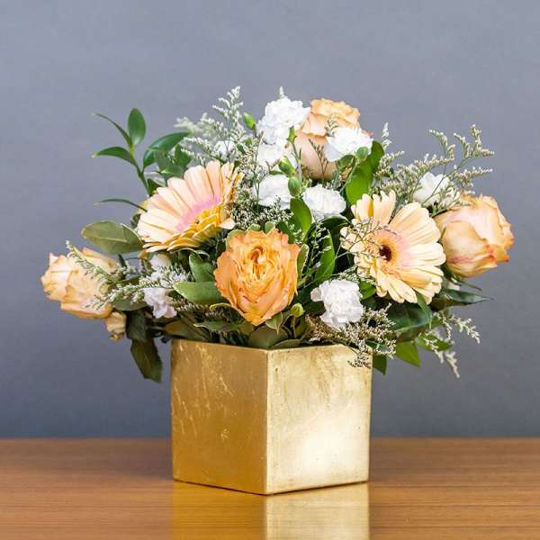 Peach and white flowers arranged in a gold square vase