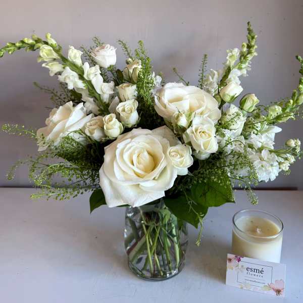 White roses and snapdragons in a glass vase beside a candle