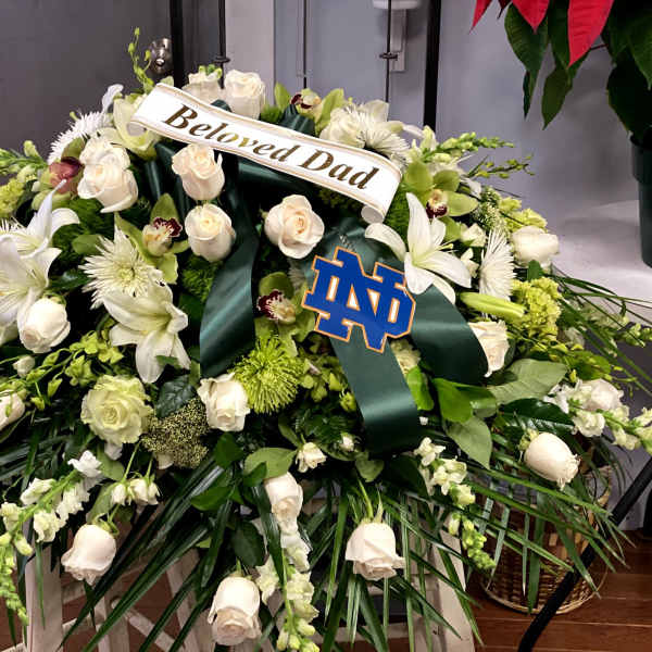 White floral funeral spray with a "Beloved Dad" ribbon and Notre Dame emblem