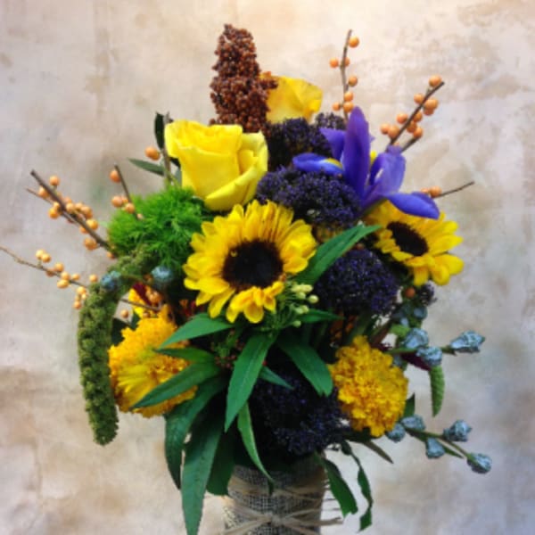 Tall bouquet of yellow roses, sunflowers, and purple flowers in a glass vase
