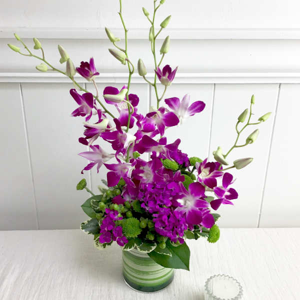 Purple orchids in a striped glass vase with green accents