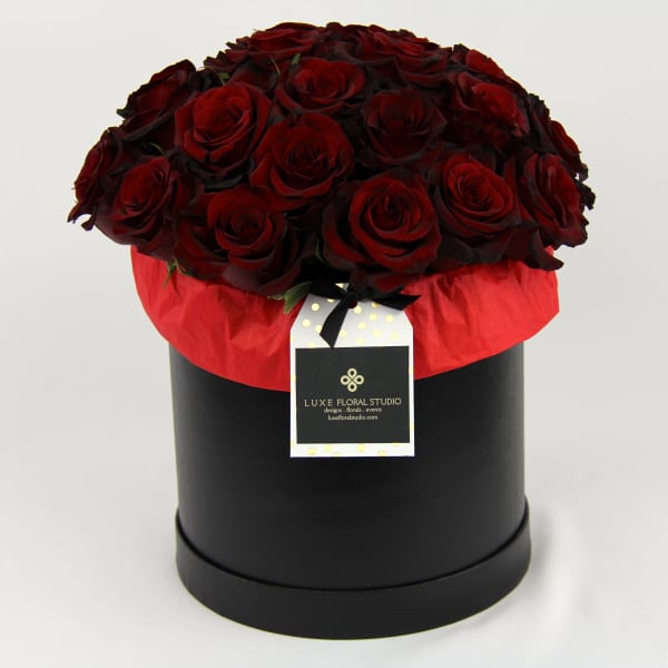 Red roses arranged in a black round box with a hanging tag